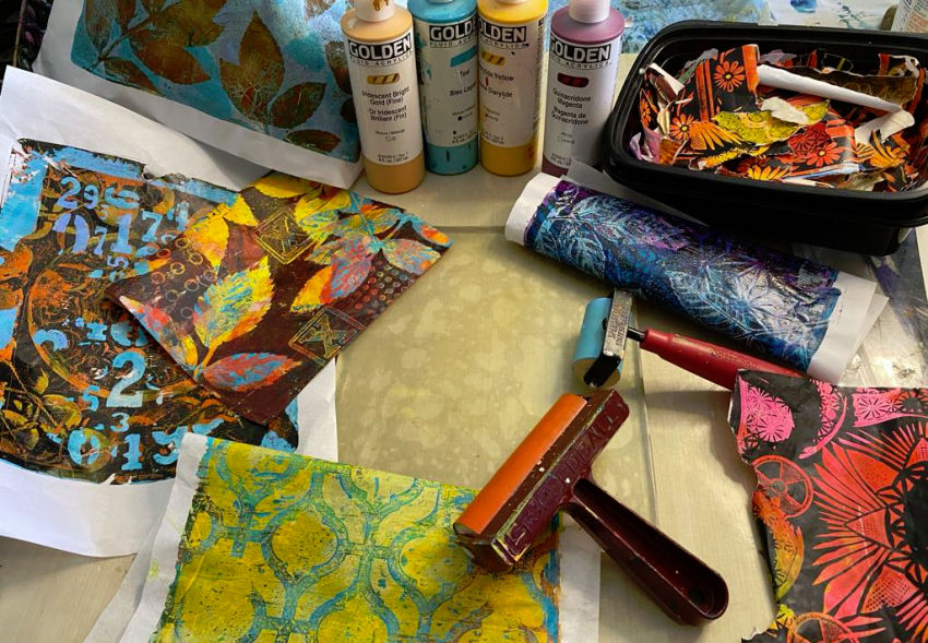 Gel printing supplies including acrylic paints, brayer, Gelli plate, and example monoprints